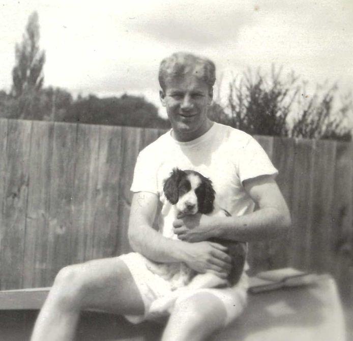 Depicts the artist Bill McCardle as a young man seated outdoors holding a small dog, possibly a Border Collie puppy